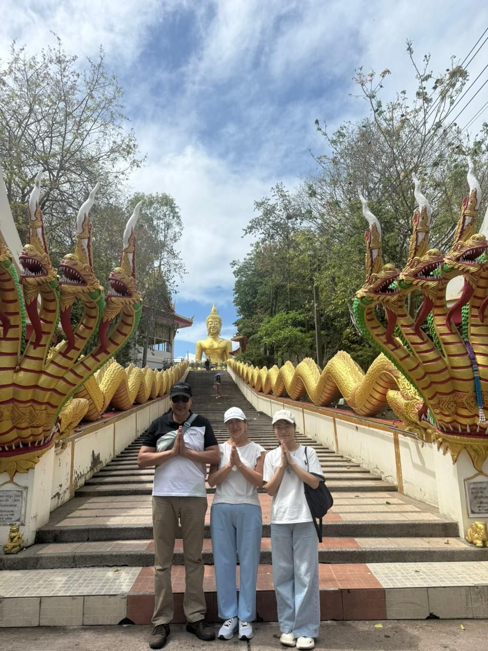 Guests greeting at a Thai temple staircase with a golden Buddha